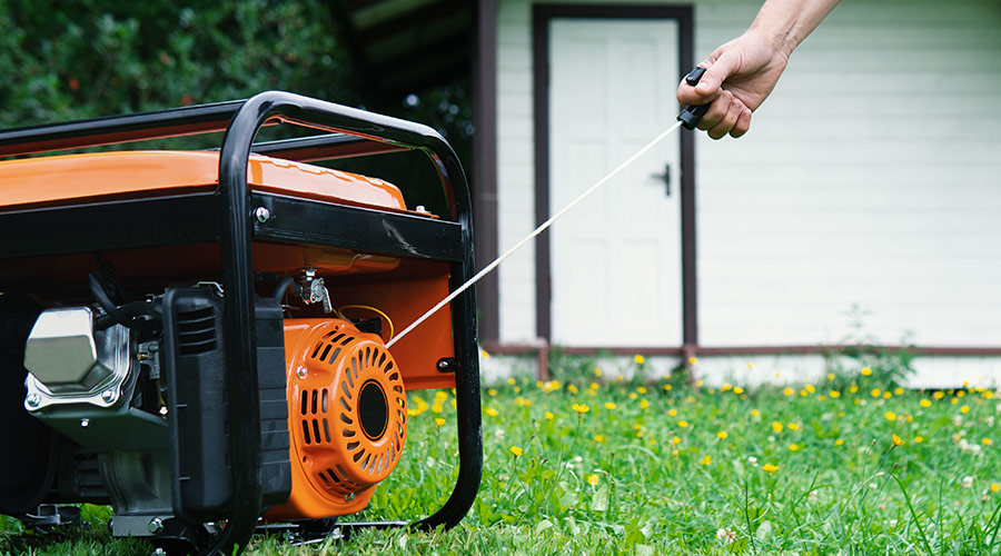 person pulling the cord on a generator which is located outdoors