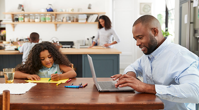 family in kitchen, father on computer while kids do homework