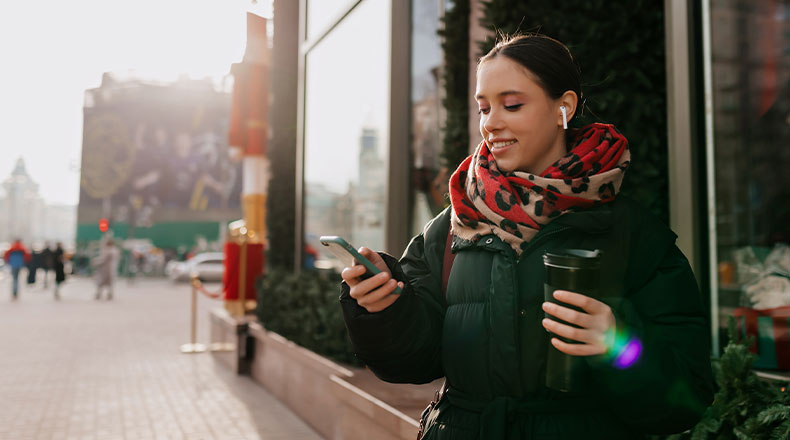 woman holding her phone outside with a coffee